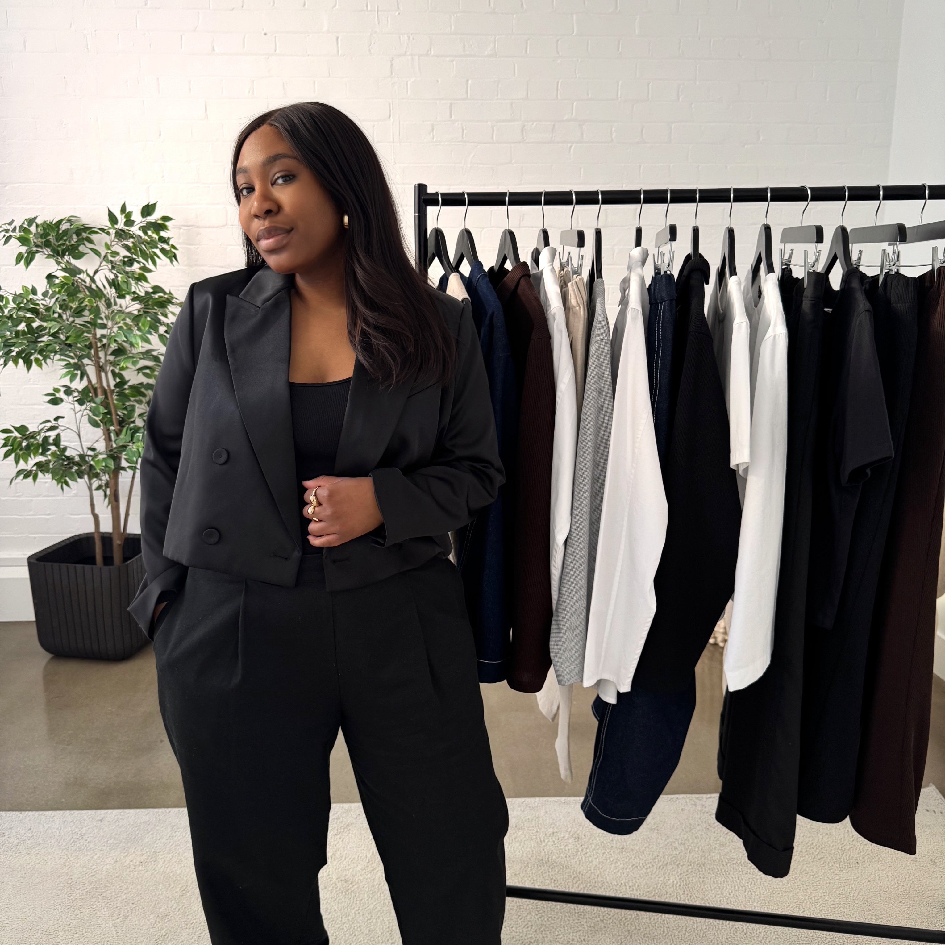 Image of Founder, Lea in a black outfit with a rail of clothing from RILEY & MONICA