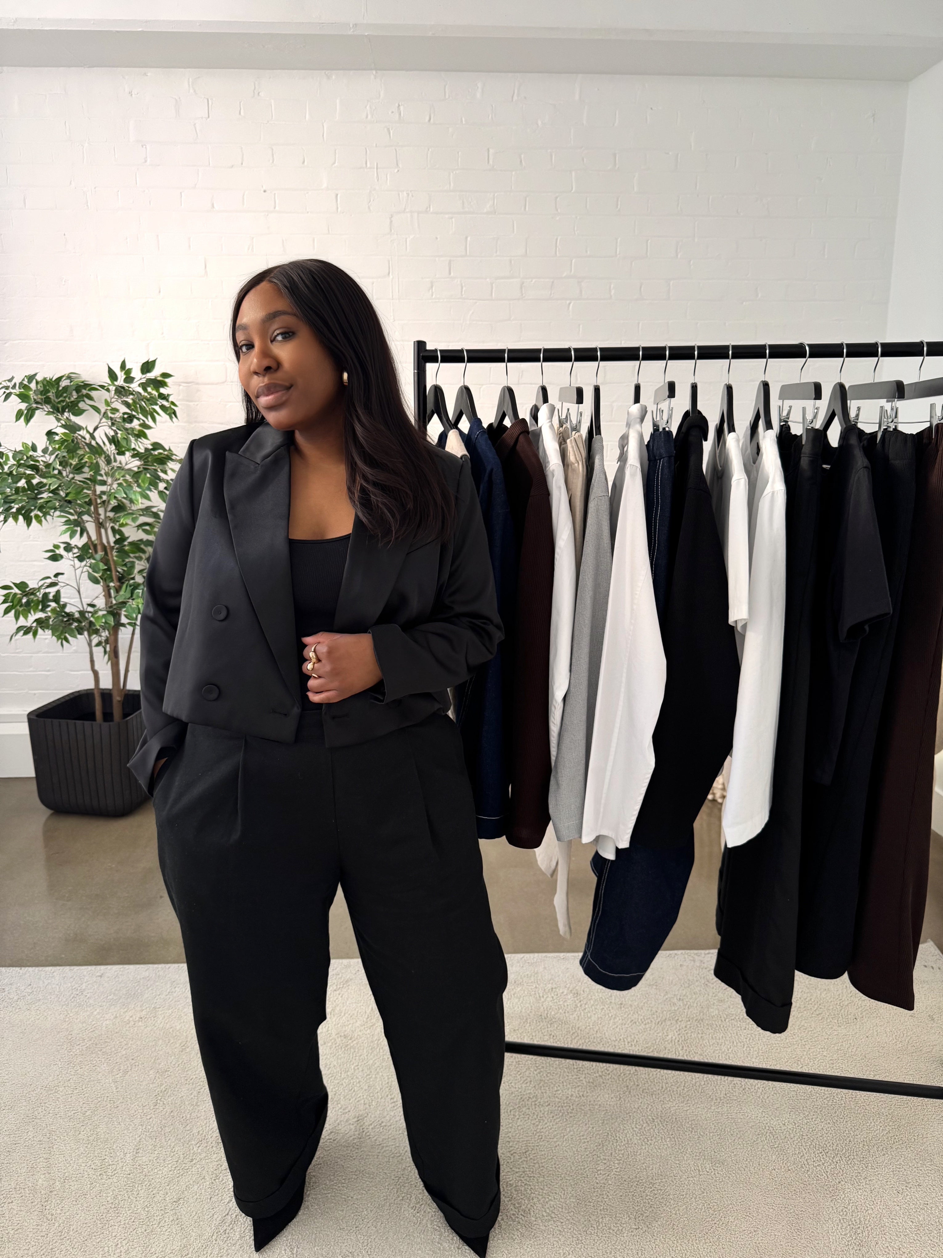 Image of Founder, Lea in a black outfit with a rail of clothing from RILEY & MONICA